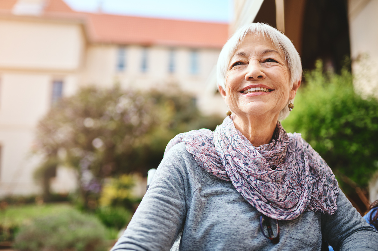 Smiling senior woman sitting outdoors in the sunshine with a patterned scarf around her neck