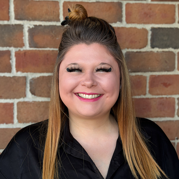 Samantha Haney, Business Office Director at Holliday Farms Senior Living, smiling in a professional headshot. She wears a black blouse, with long highlighted hair styled half up and a brick wall background.
