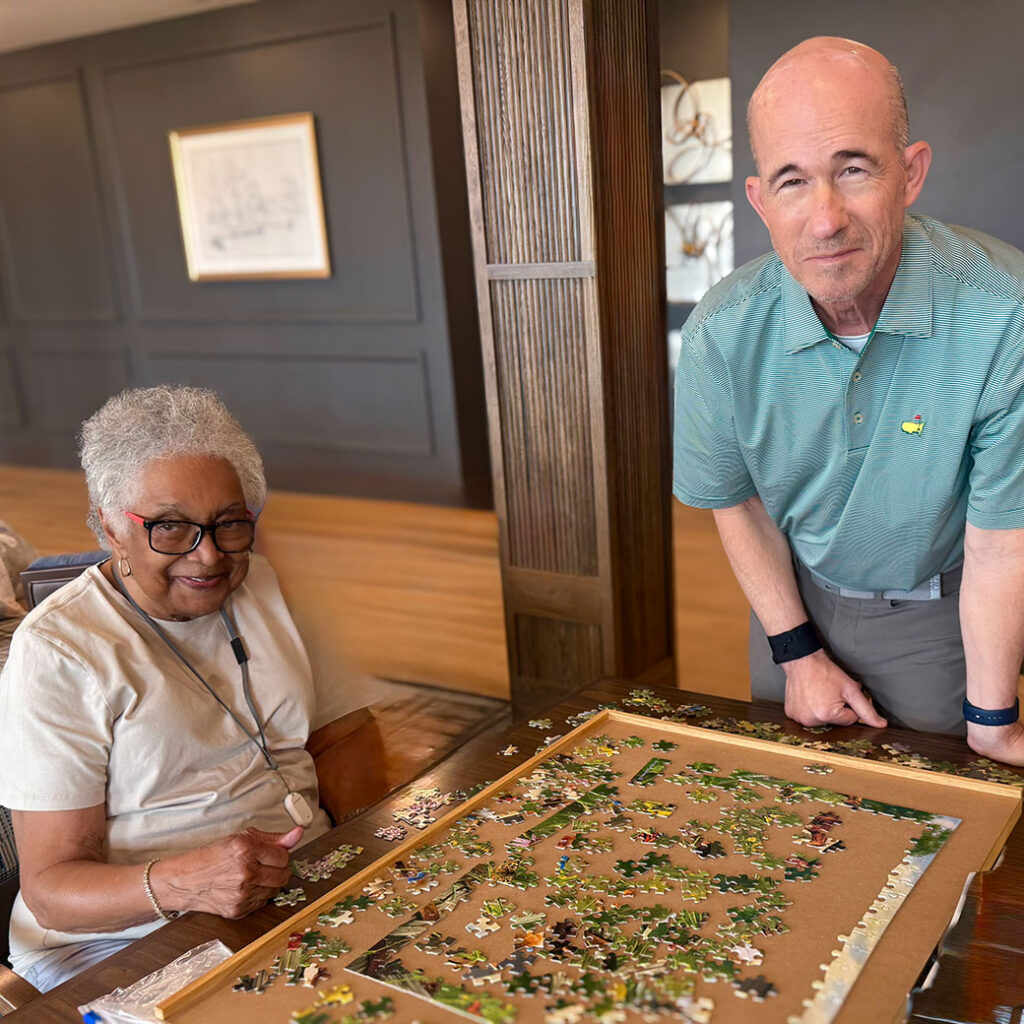 A man and woman at Holliday Farms Senior Living smile while working on a puzzle.