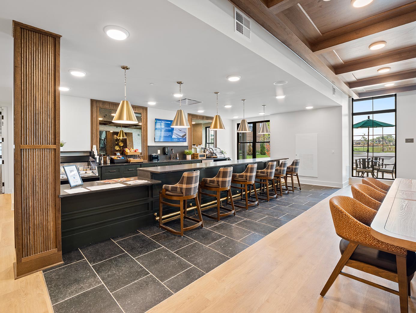 Senior living café viewed from the dining area, featuring counter seating, a beverage station, and access to an outdoor patio.