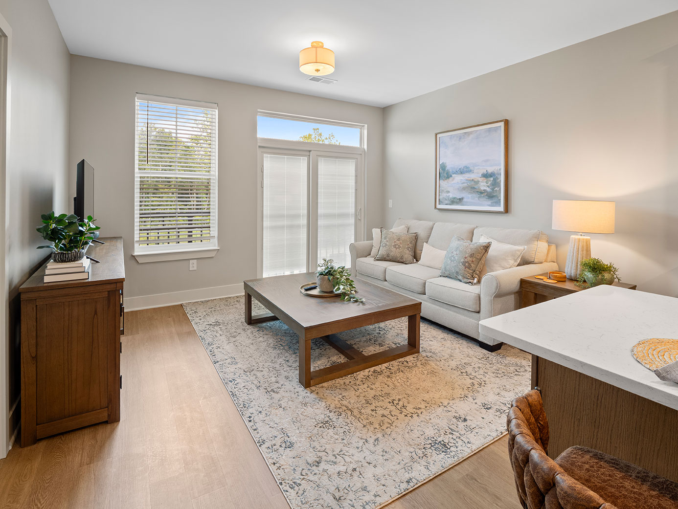 Bright senior living apartment with an open living room, sofa, television, patio doors, and a kitchen island.