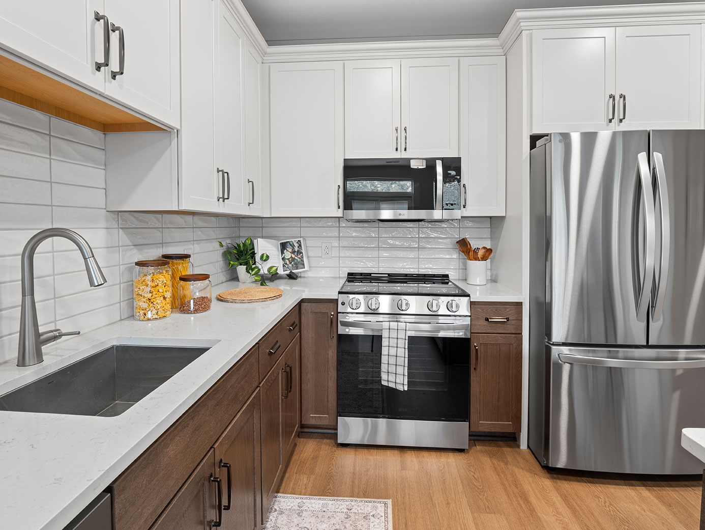 Modern senior living apartment kitchen with white and wood cabinetry, quartz countertops, and stainless steel appliances.